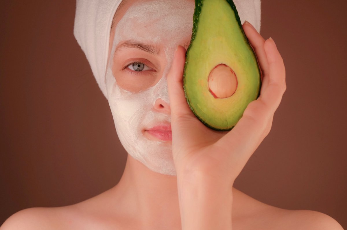 woman with cosmetic mask holding avocado